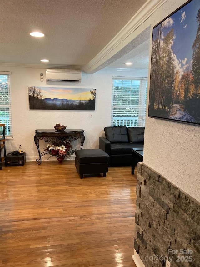 living area featuring ornamental molding, a wall mounted air conditioner, a textured ceiling, wood finished floors, and plenty of natural light