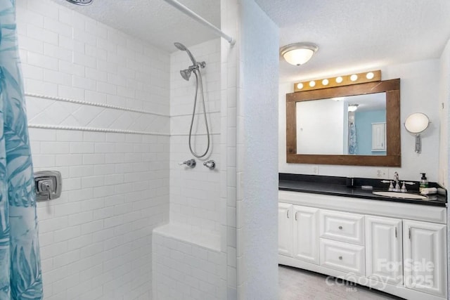 bathroom with a textured ceiling, a tile shower, and vanity