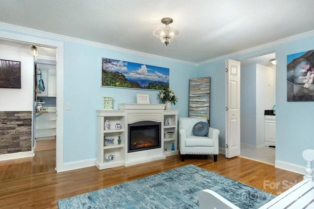 living room with wood finished floors, ornamental molding, a glass covered fireplace, and baseboards