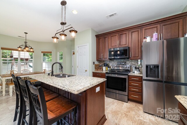 8927 Comstock Ct, Locust, NC 28097 - kitchen with appliances with stainless steel finishes, a sink, decorative backsplash, a center island with sink, and light stone counters