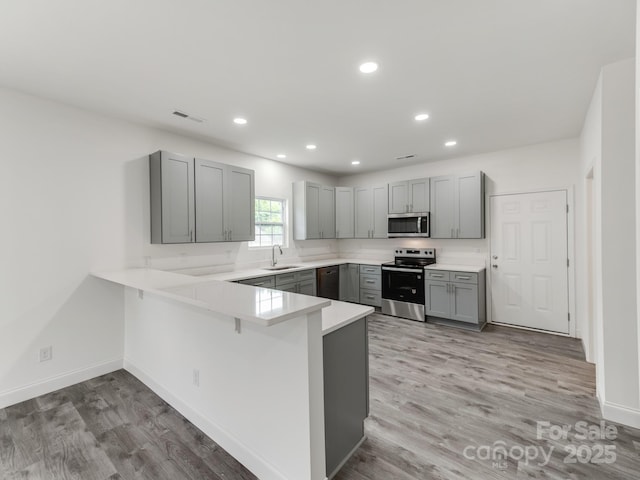kitchen featuring stainless steel appliances, a sink, gray cabinets, a peninsula, and light wood finished floors