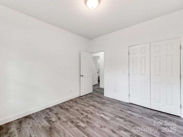 unfurnished bedroom featuring wood finished floors, baseboards, and a closet