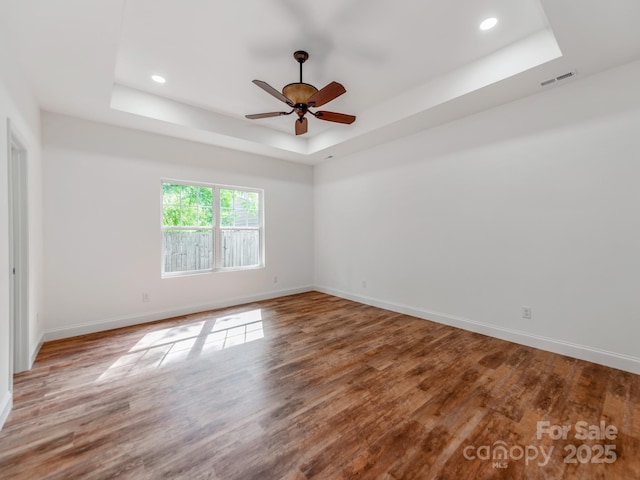 unfurnished room with a tray ceiling, wood finished floors, baseboards, recessed lighting, and ceiling fan