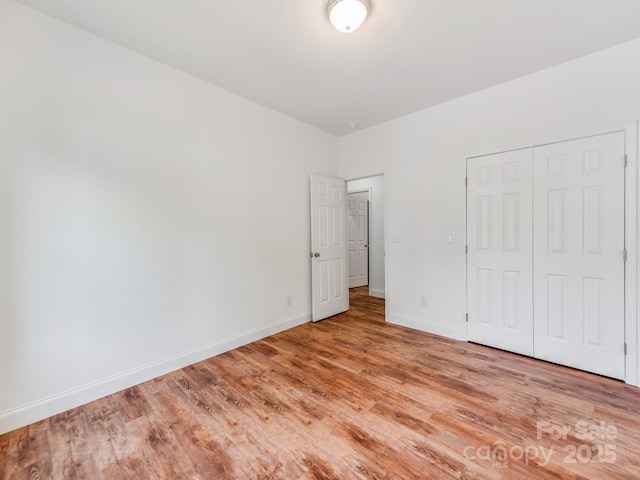 unfurnished bedroom featuring light wood finished floors, baseboards, and a closet