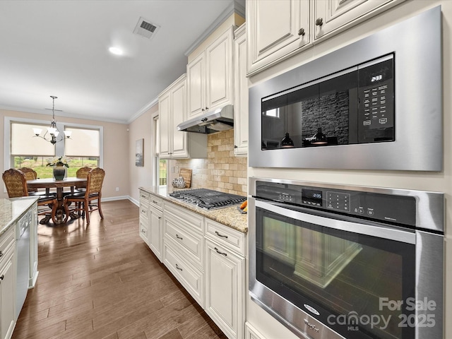 1190 Arges River Dr, Fort Mill, SC 29715 - kitchen with appliances with stainless steel finishes, under cabinet range hood, crown molding, a chandelier, and decorative backsplash