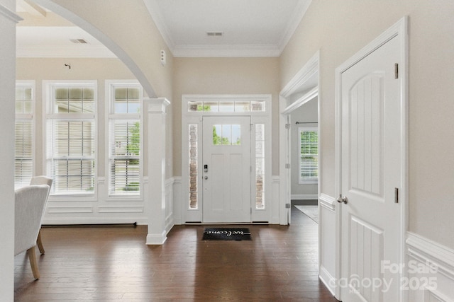 foyer featuring dark wood finished floors, ornamental molding, arched walkways, a wainscoted wall, and a decorative wall