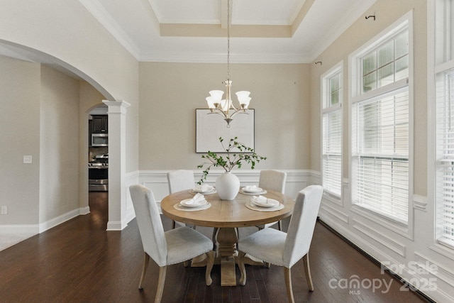 dining room featuring arched walkways, dark wood finished floors, a wainscoted wall, a chandelier, and crown molding