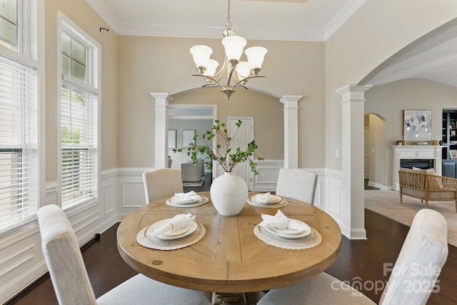 dining area with arched walkways, ornate columns, dark wood-type flooring, a chandelier, and a decorative wall