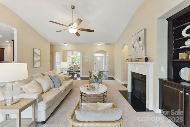 living area with arched walkways, a ceiling fan, lofted ceiling, a fireplace with flush hearth, and baseboards