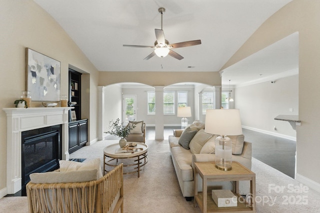 living area featuring decorative columns, arched walkways, vaulted ceiling, a ceiling fan, and baseboards