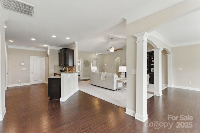 unfurnished living room with arched walkways, ceiling fan, ornate columns, dark wood-style floors, and ornamental molding
