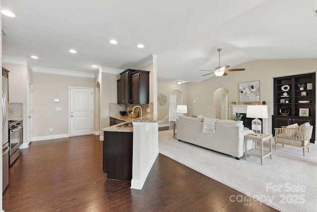 living room featuring arched walkways, ornamental molding, dark wood-style flooring, a ceiling fan, and baseboards