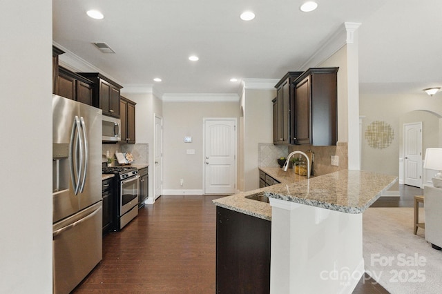 kitchen with stainless steel appliances, crown molding, dark brown cabinetry, light stone counters, and arched walkways