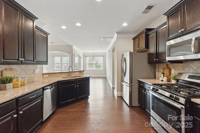 kitchen featuring stainless steel appliances, a sink, ornate columns, light stone counters, and ornamental molding