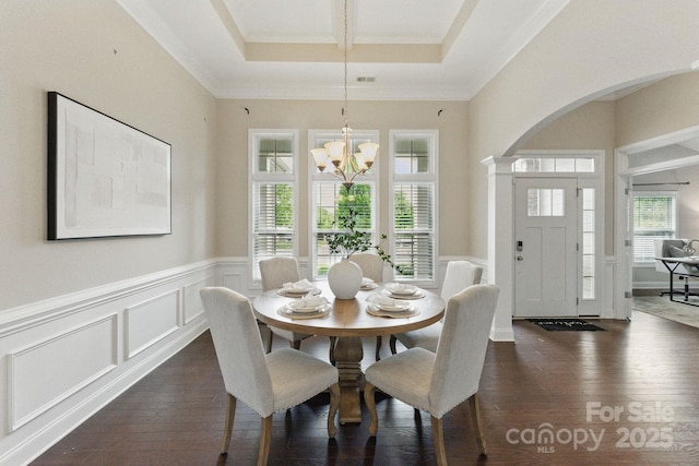 dining room with healthy amount of natural light, a chandelier, arched walkways, dark wood-type flooring, and a wainscoted wall