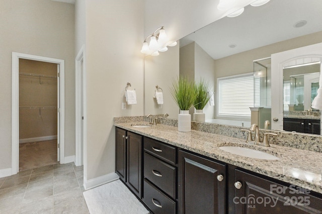 full bath featuring double vanity, a shower stall, a walk in closet, and baseboards