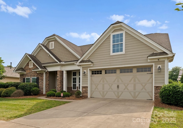 craftsman house featuring stone siding, concrete driveway, a front yard, and a shingled roof