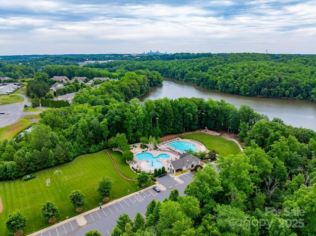 drone / aerial view of a large body of water, a pool area, and a forest
