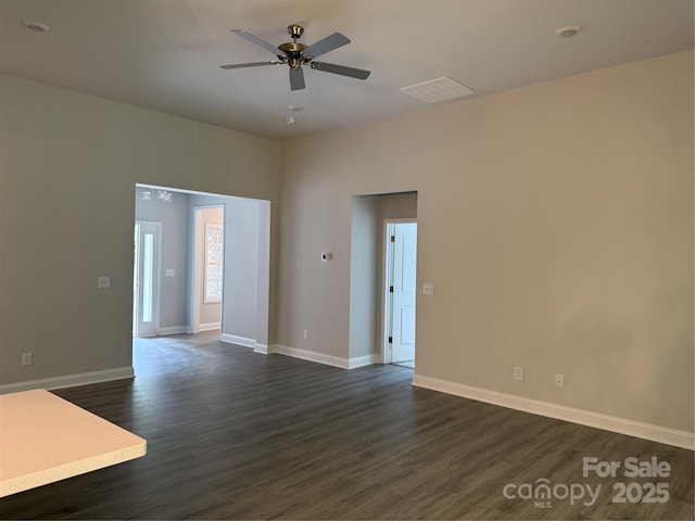 spare room featuring dark wood-type flooring, a ceiling fan, and baseboards