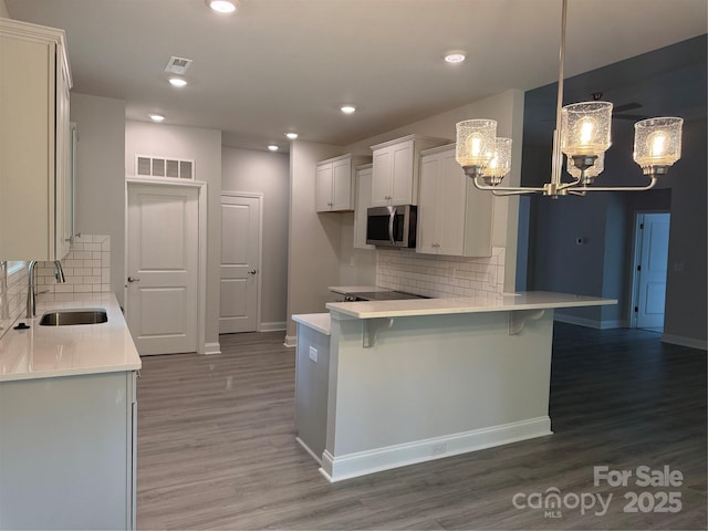 kitchen featuring a sink, stainless steel microwave, a chandelier, a kitchen breakfast bar, and wood finished floors