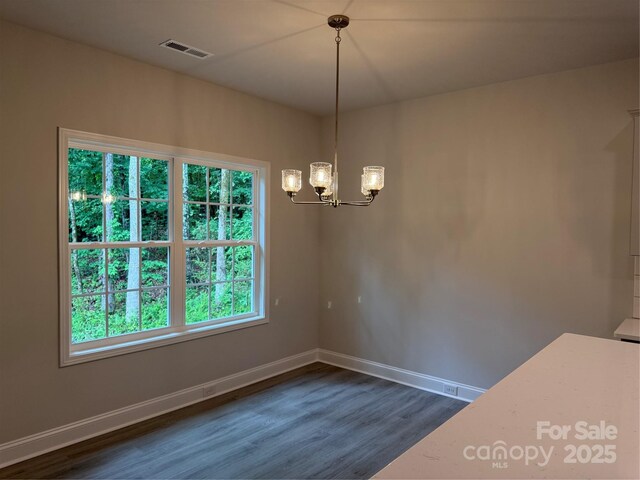 unfurnished dining area featuring dark wood-style floors, a chandelier, and baseboards