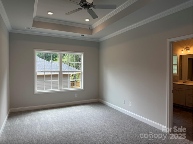 unfurnished room with a raised ceiling, carpet, a ceiling fan, crown molding, and baseboards
