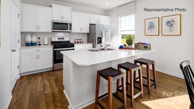 kitchen with stainless steel appliances, a sink, a breakfast bar area, backsplash, and dark wood-style flooring