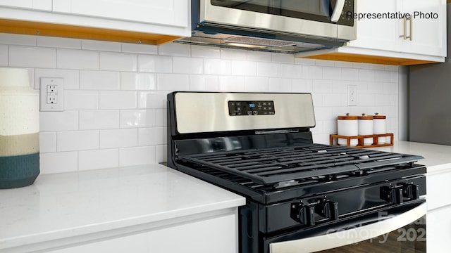 kitchen view of stainless steel appliances, backsplash, white cabinetry, and light stone counters