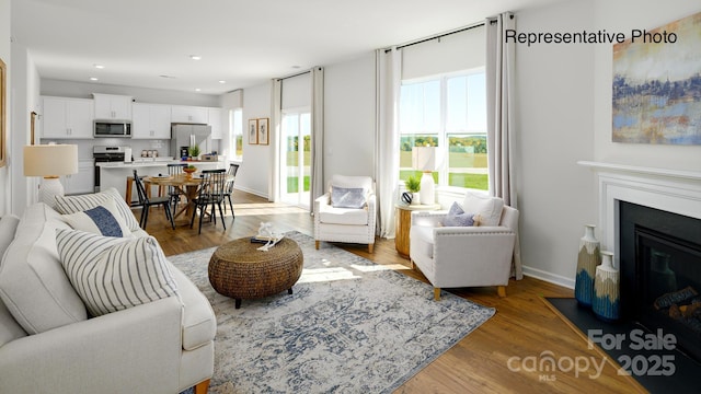 living area with light wood-style floors, a fireplace with flush hearth, recessed lighting, and baseboards