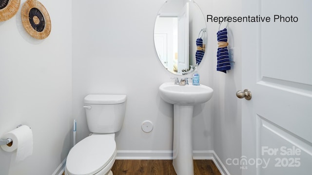 half bath featuring toilet, baseboards, wood finished floors, and a sink