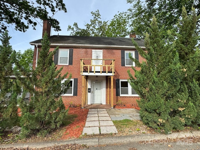 view of front facade featuring a balcony, a chimney, and brick siding
