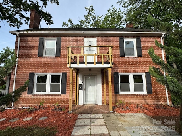 view of property with a balcony, a chimney, and brick siding