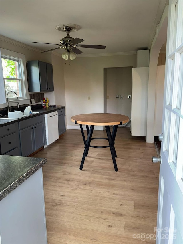 kitchen with dishwasher, crown molding, dark countertops, a sink, and a ceiling fan