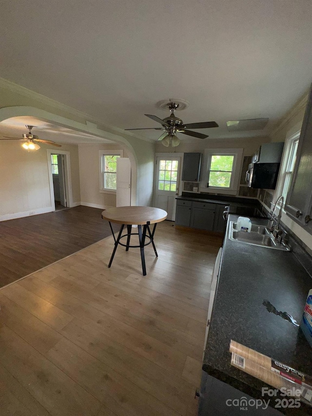 kitchen with ceiling fan, a sink, arched walkways, dark countertops, and wood finished floors