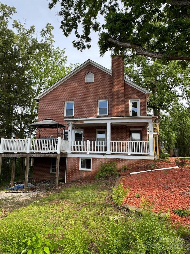 back of house featuring a chimney, brick siding, and a wooden deck