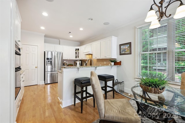 3128 Ethereal Ln, Charlotte, NC 28226 - kitchen featuring stainless steel appliances, a peninsula, ornamental molding, light stone countertops, and white cabinets