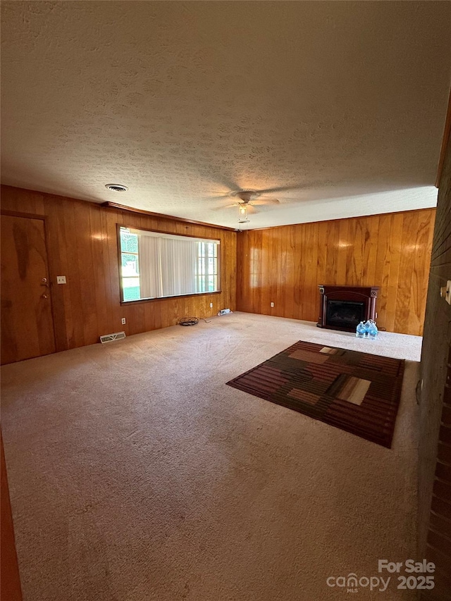 unfurnished living room with wood walls, a fireplace, a textured ceiling, carpet, and a ceiling fan