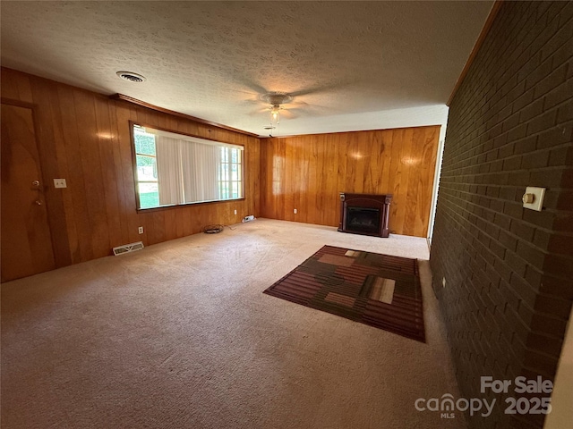 unfurnished living room with a textured ceiling, ceiling fan, wooden walls, carpet floors, and a fireplace