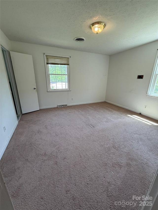 empty room featuring a textured ceiling, carpet floors, and baseboards