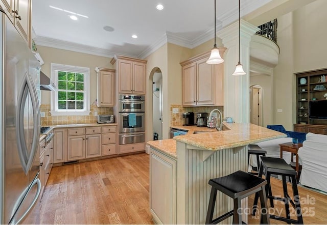 kitchen with appliances with stainless steel finishes, arched walkways, a warming drawer, a sink, and light brown cabinets