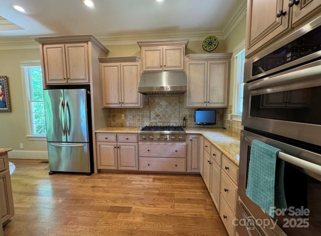 kitchen with appliances with stainless steel finishes, under cabinet range hood, ornamental molding, light wood-type flooring, and decorative backsplash
