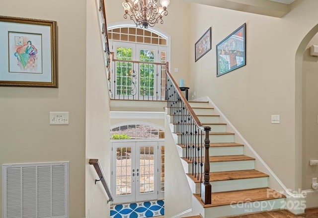 stairway featuring french doors, a towering ceiling, arched walkways, and a chandelier