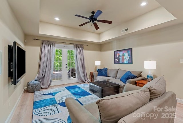 living room with a raised ceiling, french doors, wood finished floors, baseboards, and ceiling fan