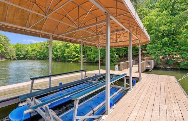 dock with boat lift, a water view, and view of scattered trees