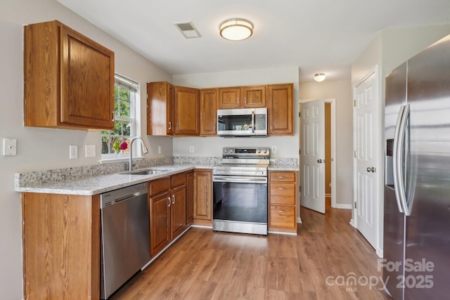 6332 Sackett Way, Charlotte, NC 28269 - kitchen with stainless steel appliances, a sink, light wood-style flooring, and brown cabinetry