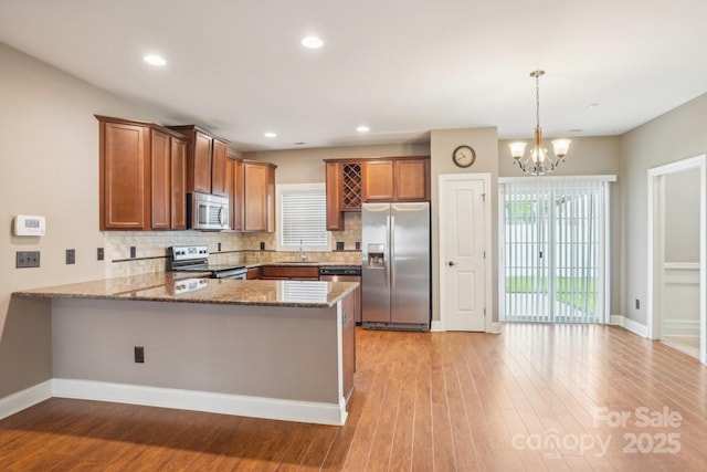 2021 Chantilly Ln, Salisbury, NC 28146 - kitchen featuring appliances with stainless steel finishes, a peninsula, brown cabinetry, light stone counters, and backsplash
