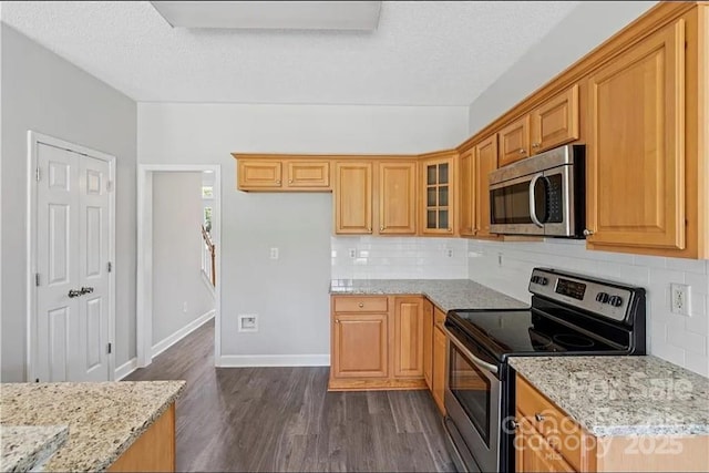kitchen with appliances with stainless steel finishes, dark wood-type flooring, backsplash, light stone countertops, and a textured ceiling