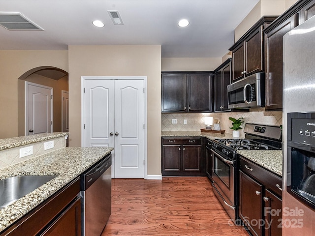 7325 Overmountain Dr, Rock Hill, SC 29732 - kitchen featuring appliances with stainless steel finishes, arched walkways, wood finished floors, light stone counters, and decorative backsplash