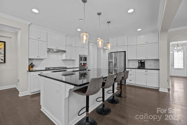 2414 Madeira Cir, Waxhaw, NC 28173 - kitchen with appliances with stainless steel finishes, dark countertops, arched walkways, under cabinet range hood, and white cabinetry