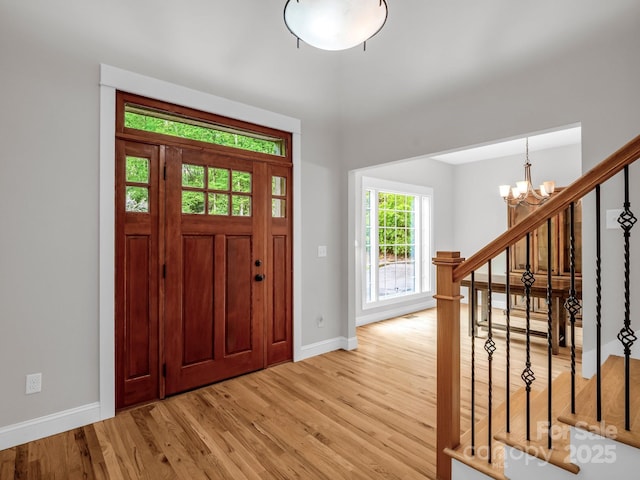 entryway featuring a chandelier, baseboards, light wood-style floors, and stairs